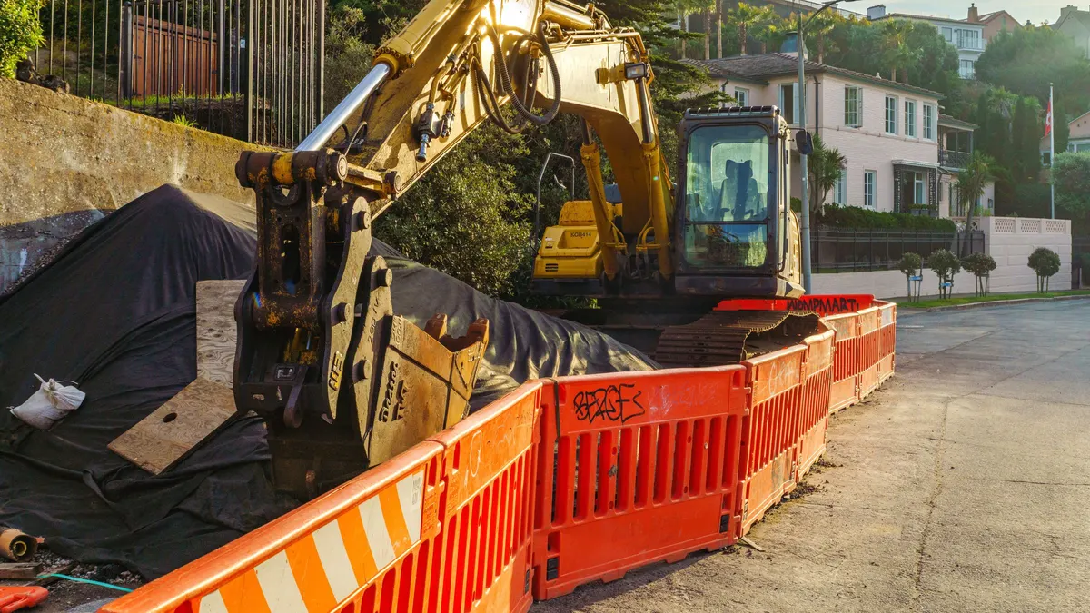 Excavator digging beside a residential street with orange safety fencing